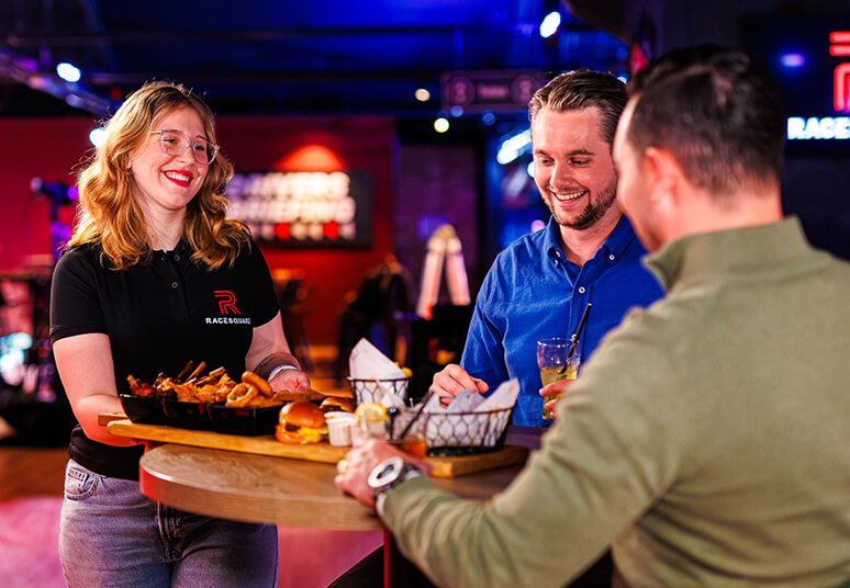 Medewerker van Racesquare serveert hapjes aan twee bezoekers tijdens een borrelmoment in de bar.